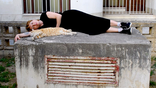 woman in black laying together with yellow tabby cat in street