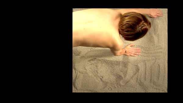 bare skinned woman pulling hand through sand